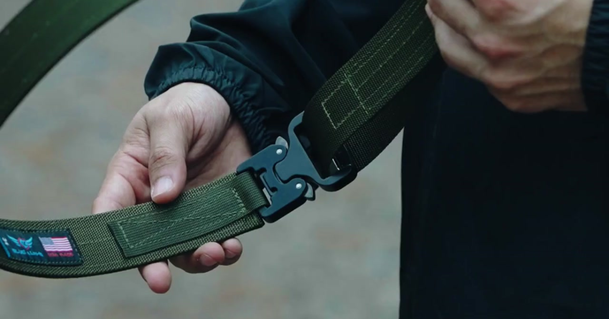 A man holding a green Blue Alpha EDC belt.