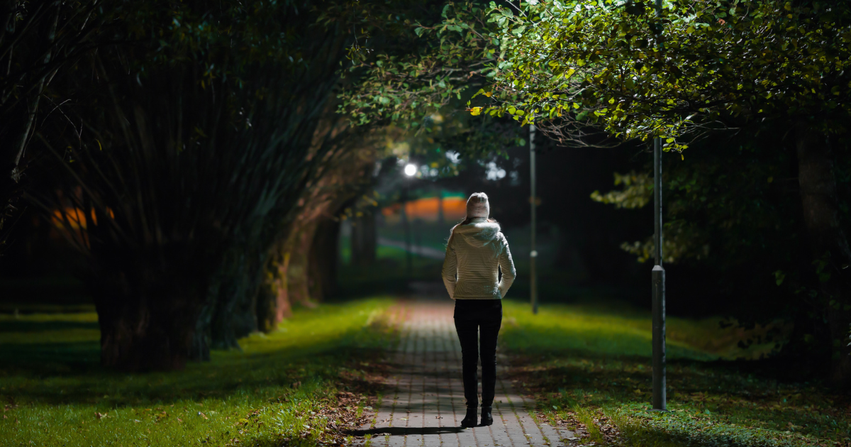 A woman in a white hoodie walking alone in the dark.