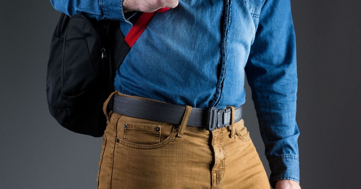 A man in work pants and a casual button down shirt carrying a backpack and wearing a Blue Alpha EDC Belt.