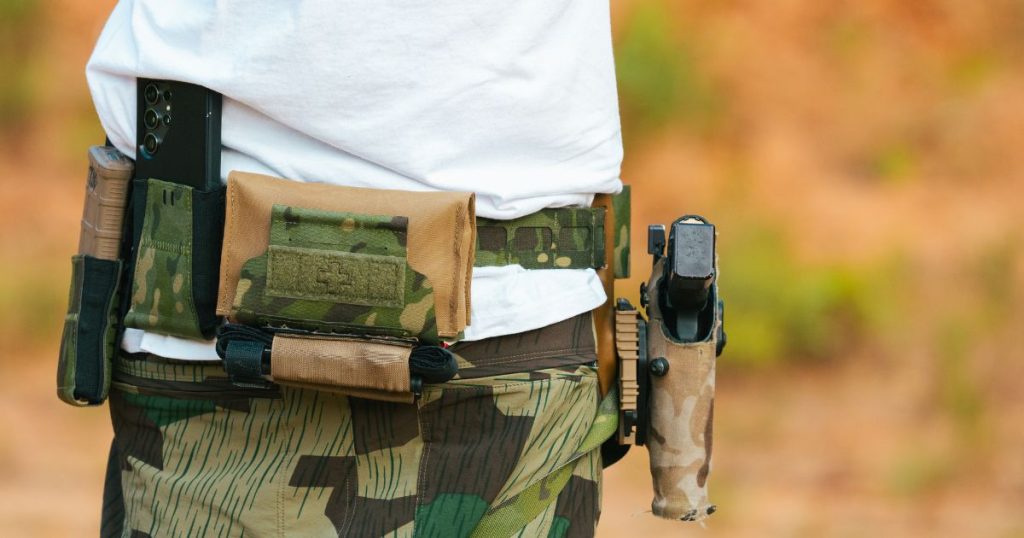 A man wearing a Blue Alpha Medical Pouch on his battle belt using the up pull tab method.