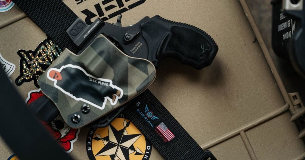 A handgun on an Blue Alpha EDC belt against a brown background.