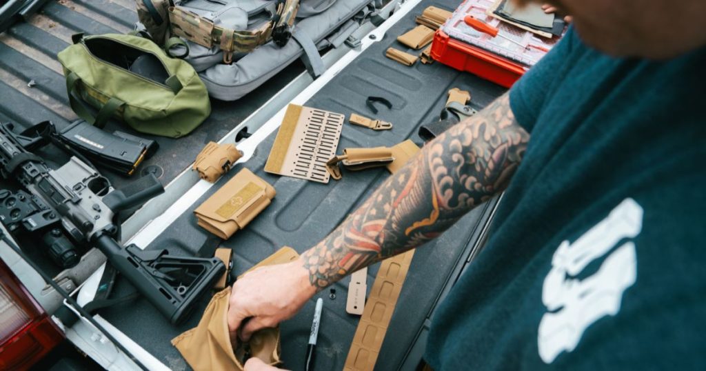 A man adding gear to his battle belt with it all laid out on his truck bed.