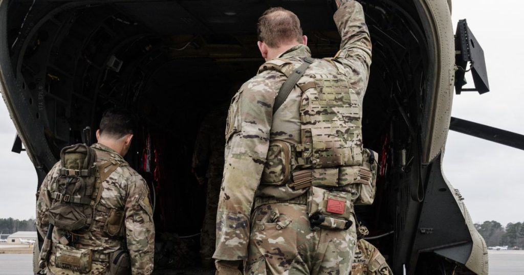 A man standing wearing a plate carrier with rear magazines next to a plane.