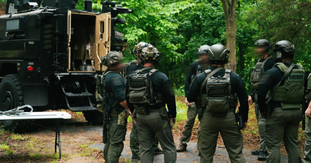 Men wearing plate carriers and helmets standing in a forest.