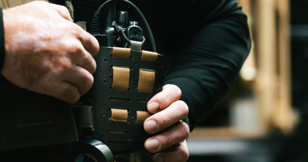 A person adjusting their plate carrier wing adapter that is holding a radio.